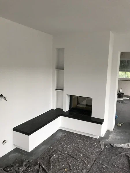 Verputzter deckenhoher Heizkamin mit großer Sitzbank aus nero Assoluto Naturstein
